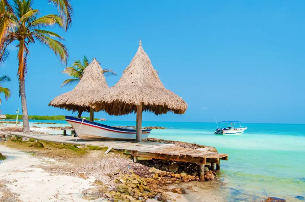 Rustic pier with thatched huts and fishing boats on turquoise Caribbean sea at Rincón del Mar, Colombia